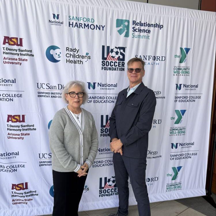 Two attendees stand in front of the partner logo backdrop at the Sanford Relationship Science Summit
