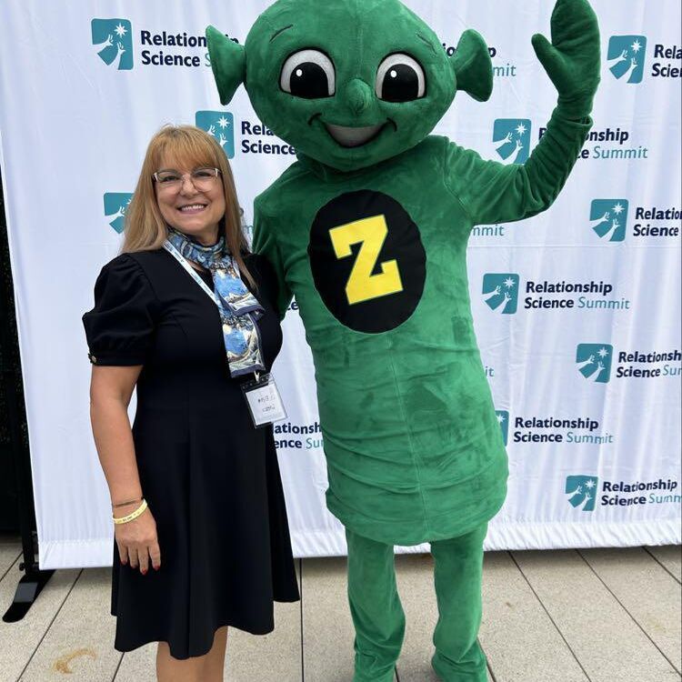 An attendee waves alongside the Sanford Harmony mascot in front of the summit backdrop