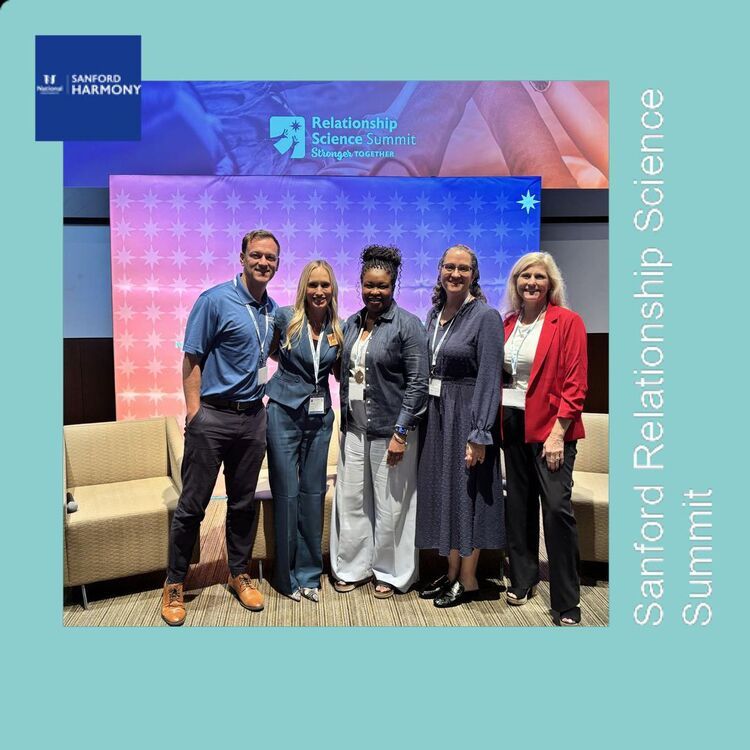 Five attendees pose together in front of the summit stage backdrop
