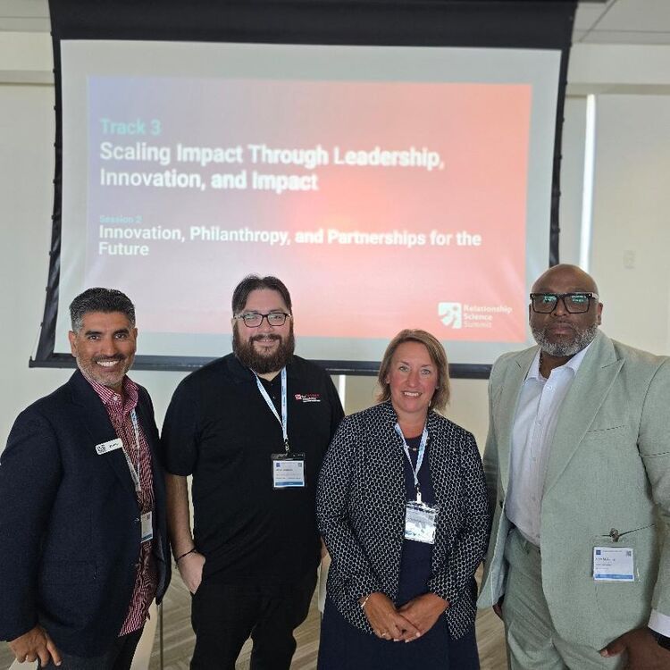 Four attendees pose in front of a Track 3 session slide on scaling impact through leadership and innovation